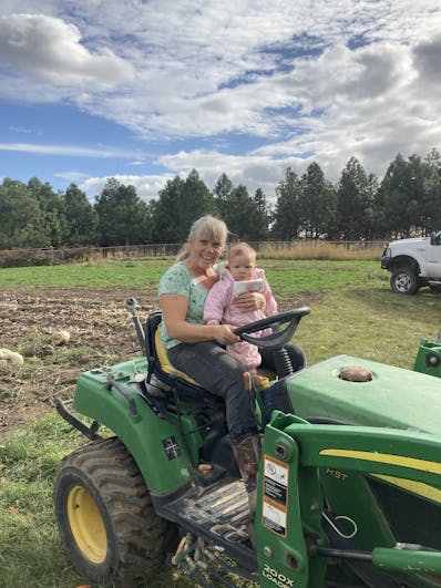 Michelle Stelzer holding a baby sitting on a mower near a garden